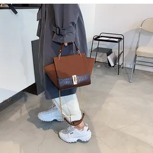 Detail showing mixed-texture handbag with metal chain and handle on a fashion model