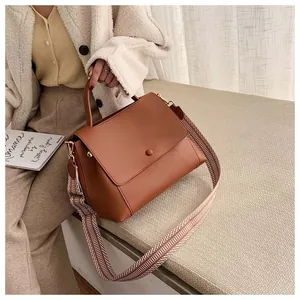 Detail of brown leather handbag with geometric patterned wide strap in a home setting