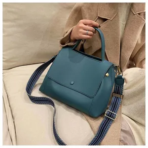 Detail of teal leather handbag featuring a wide blue geometric patterned woven strap