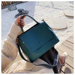 Deep green leather tote bag with stylish striped woven shoulder strap on a sunlit terrace