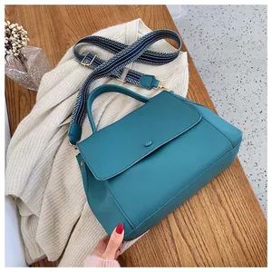 Detail of teal leather handbag with decorative blue and white woven shoulder strap