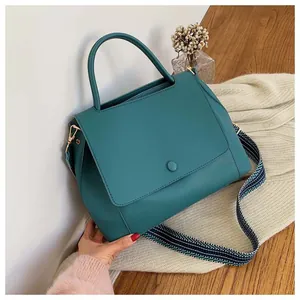 Detail of dark teal leather tote with textured woven strap on elegant wooden surface