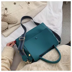 Detail of teal leather handbag featuring a geometric striped strap and gold metal buckles
