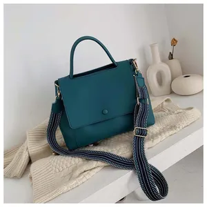 Detailed view of dark teal leather handbag with striped wide strap and magnetic closure