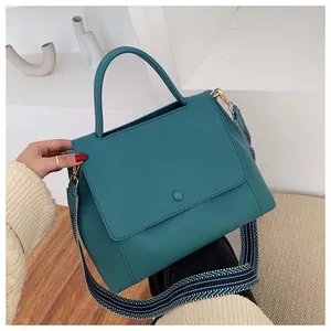 Detail of teal leather handbag featuring a wide blue and white striped fabric strap