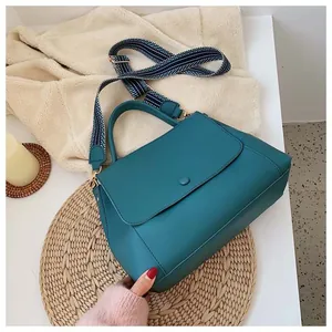 Close-up of teal leather handbag with textured surface and geometric woven shoulder strap