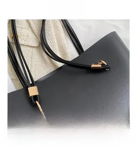 Close-up of black leather tote bag featuring gold logo and metallic strap hardware
