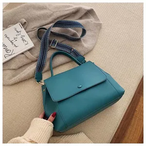 Detail of teal leather handbag with striped woven shoulder strap on knit background