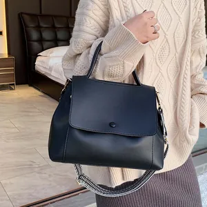 Minimalist black leather tote bag with stylish wavy shoulder strap shown in a cozy setting