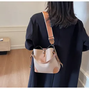 Detail view of contrast color bucket bag with wide textile strap and pebble leather texture