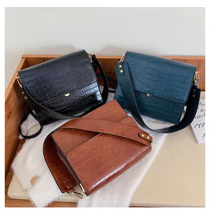 Drei strukturierte Taschen mit Krokodilmuster in Schwarz, Grün und Braun auf einem Holztablett