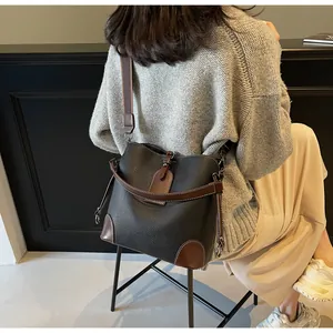 Detail of black pebbled leather bucket bag with brown trim shown on a person