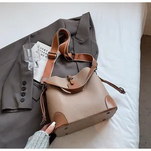 Detail of khaki bucket bag with brown leather trim and wide striped fabric strap