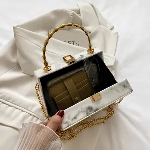 Detail view of marble print box bag with gold bamboo handle and compact interior storage