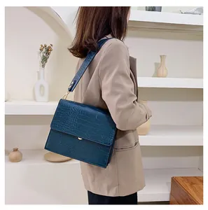 Detail der petrolfarbenen Kroko-Tasche mit Goldschließe an der Schulter des Models