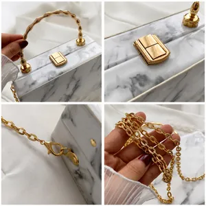 Detailed view of marble pattern clutch with gold bamboo handle and metallic chain strap