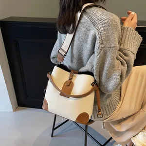 Fashionable beige and brown bucket bag with wide strap worn as a crossbody bag