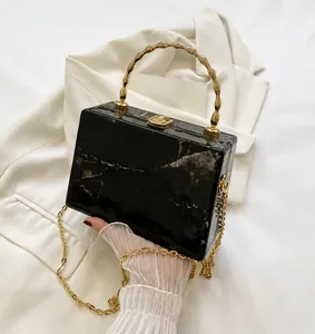 Detail of black marble box clutch with gold bamboo handle and chain on white suit
