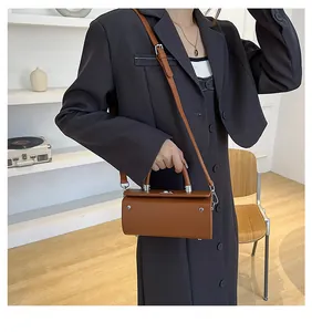 Brown cylindrical crossbody bag with silver hardware shown on model shoulder