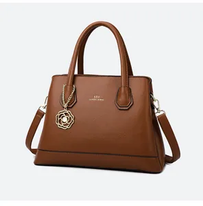 Detail of brown litchi leather handbag with gold floral pendant and branding