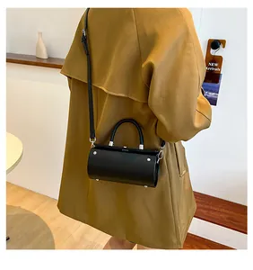 Fashionable black cylindrical mini handbag with silver buckle shown on a camel coat