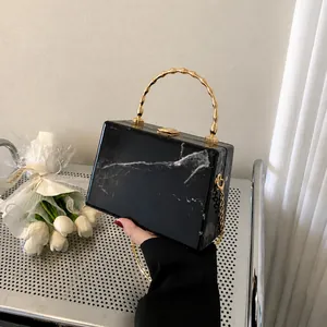 Detail view of marble pattern box bag with golden bamboo handle and chain strap