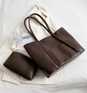 Detail of coffee brown crocodile pattern tote bag with matching pouch on clean background