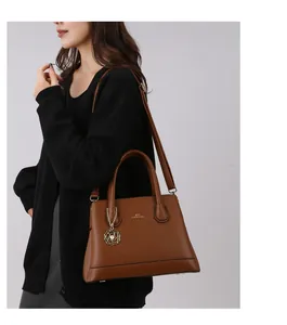 Detail of brown leather tote bag with gold charm and adjustable shoulder strap