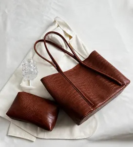Close-up of brown crocodile texture tote bag with matching pouch on white fabric