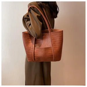 Detail showing caramel brown tote bag with crocodile embossing and long shoulder straps