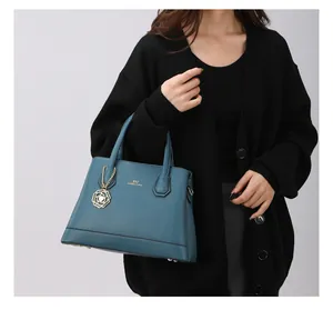 Detail of dark teal pebble leather tote bag with gold logo and floral charm accent