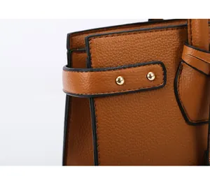 Dettaglio della borsa in pelle marrone con trama litchi, rivetti dorati e bordi neri