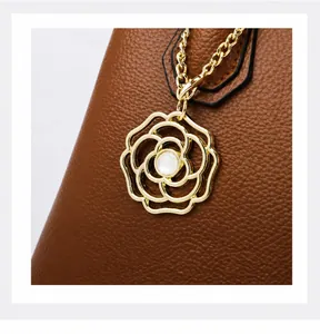Detail of brown leather tote bag with golden camellia flower charm and white pearl accent