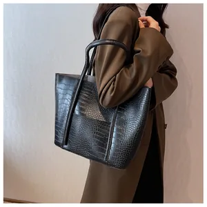 Side view of a black crocodile-textured tote bag with dual straps and front pocket detail