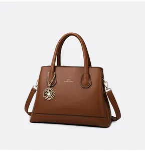 Detail of dark brown leather tote with golden floral pendant and brand lettering