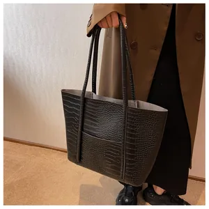 Detailed view of black tote bag with crocodile texture and double straps on a model