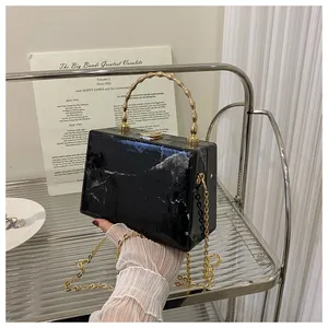 Detail of black marble box bag with golden bamboo handle and metal chain strap