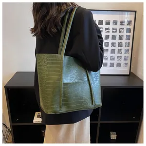 Detail of dark green crocodile embossed tote bag with slim shoulder straps on a model