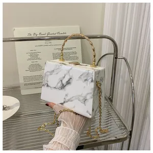 Close-up of marble pattern box clutch with golden handle held by gloved hand
