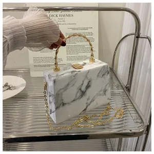 Detailed close-up of marble pattern clutch with gold wave handle and metal chain strap