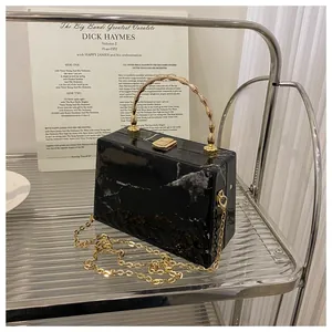 Detail of black marble box bag with golden bamboo handle and fine chain strap