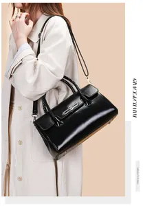 Detail of black glossy leather crossbody bag with braided handle and silver buckle on model