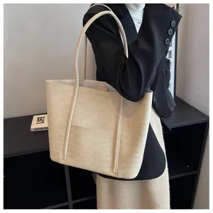 Detail view of large cream tote bag with crocodile texture worn over the shoulder
