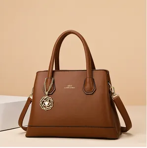 Close-up of brown pebbled leather tote bag with golden flower charm and branding