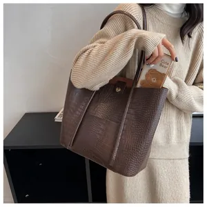 Detail of dark brown tote bag featuring crocodile texture and long shoulder straps
