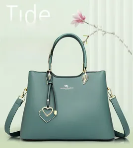 Detail of teal faux leather handbag with litchi texture and metal heart pendant