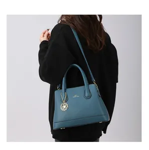 Detail of blue textured leather tote bag with gold floral charm and shoulder strap