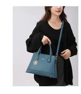Detail of teal tote bag with gold lettering and a floral charm on a model