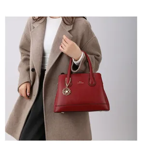 Detail of dark red leather tote bag with gold floral charm and textured finish on camel coat