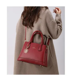 Detail of red pebble leather tote bag with gold flower charm on a camel coat model